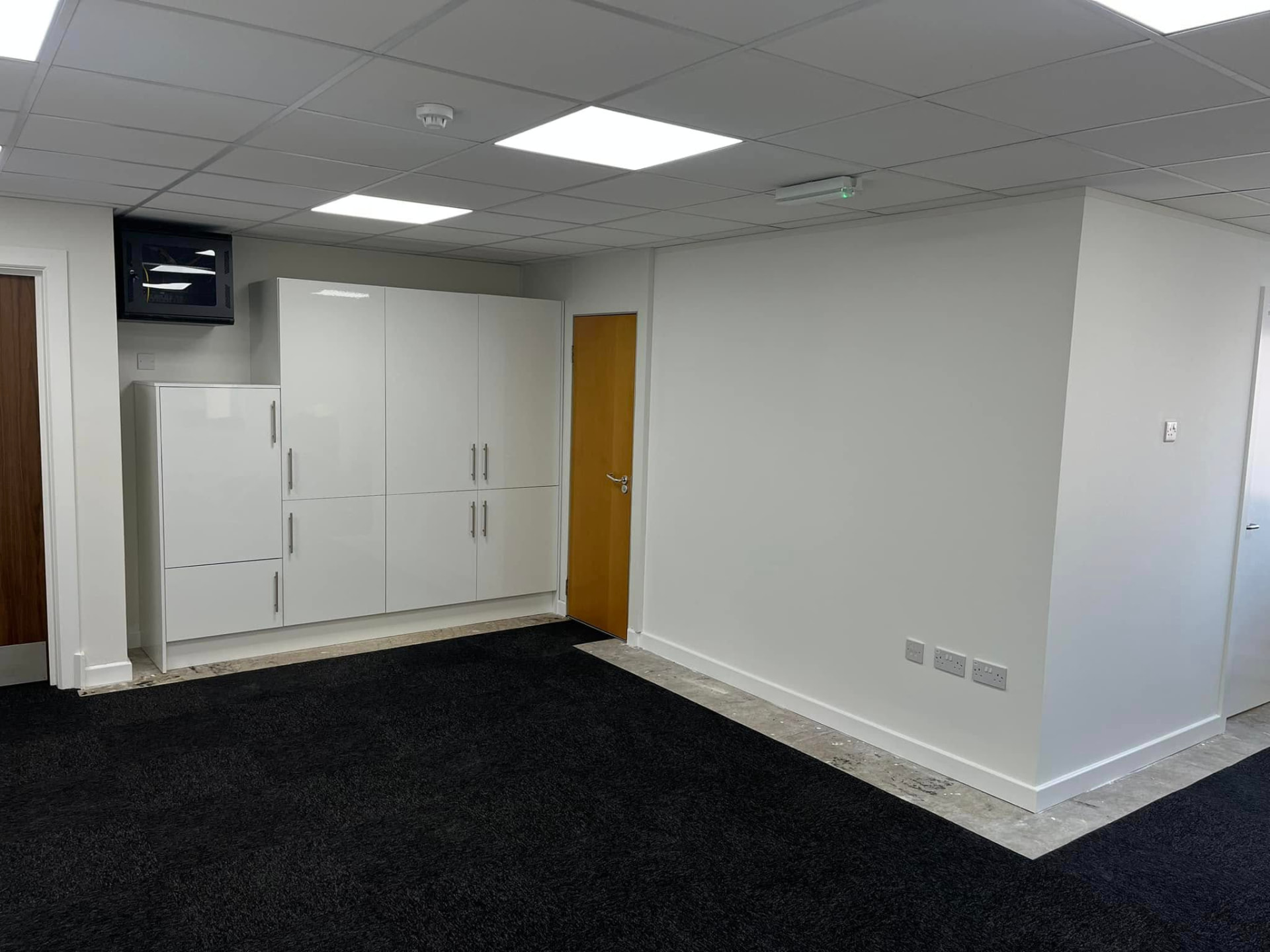 Office interior with white fitted storage cabinets, suspended ceiling and wooden door