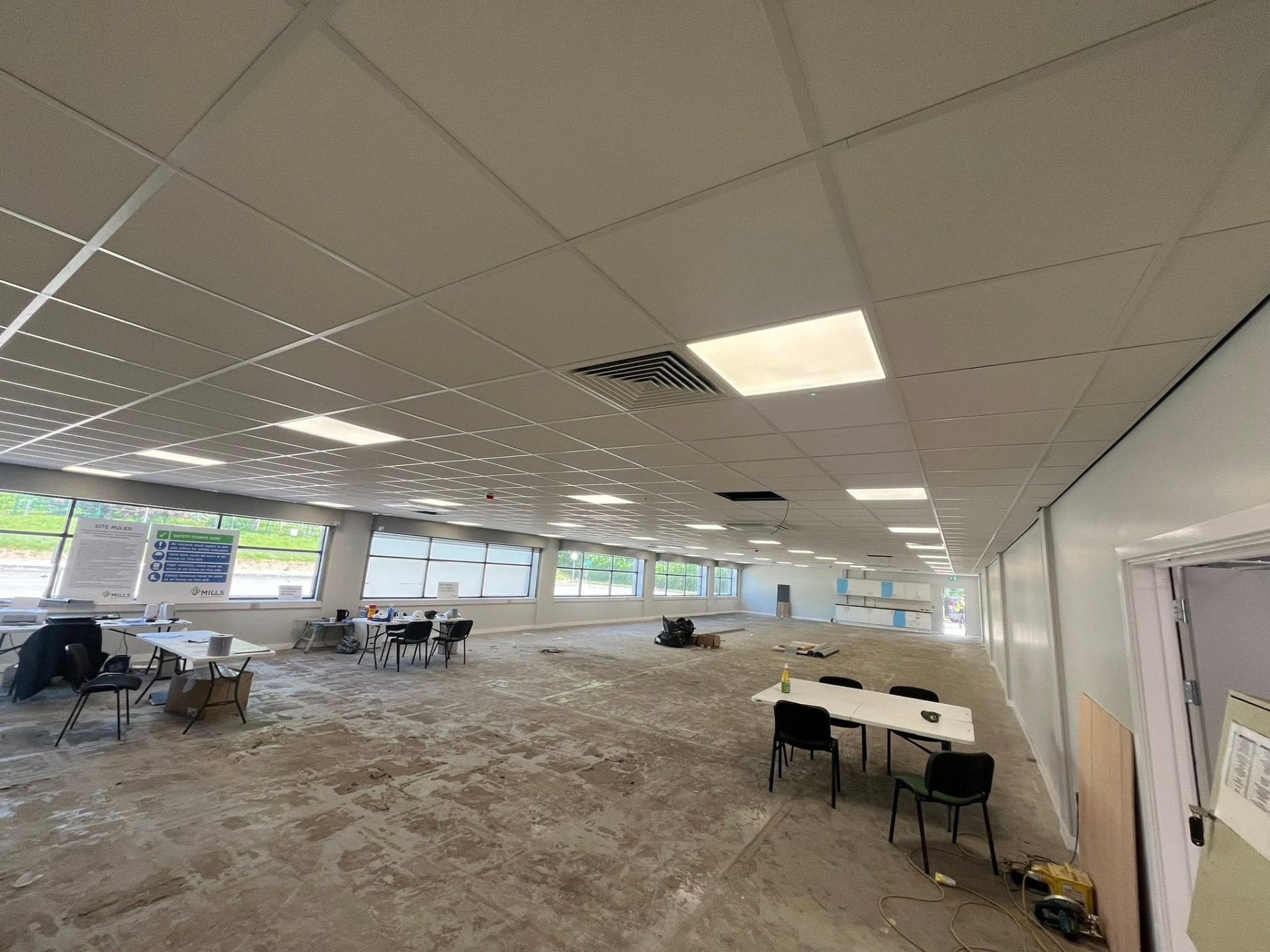 Large open-plan commercial office interior during fit-out, showing suspended ceiling grid and integrated lighting